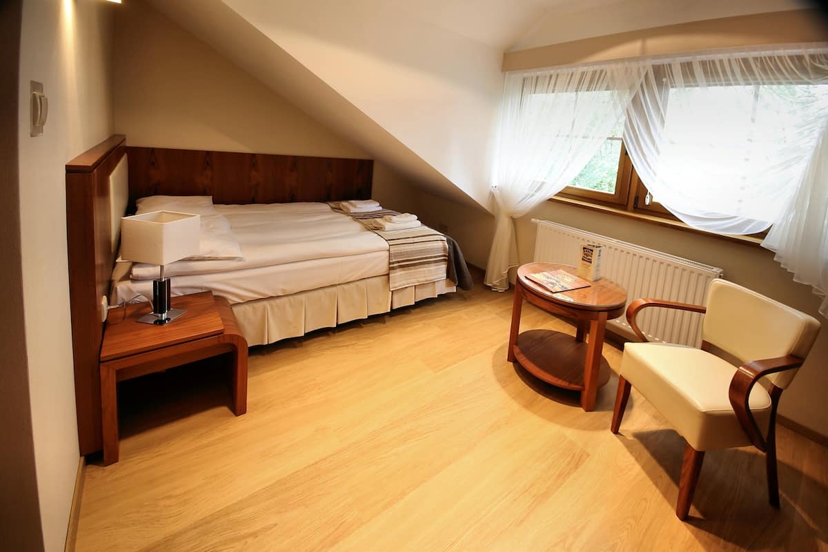 Un dormitorio con cama, mesita de noche, silla y ventana con cortinas.