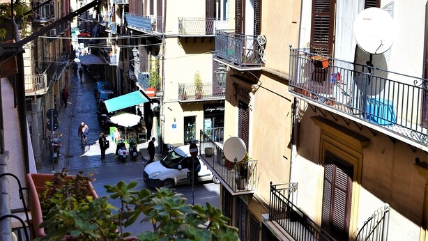 A narrow street with buildings on both sides, balconies, and a few pedestrians. - Hostel Via Zara (Palermo)