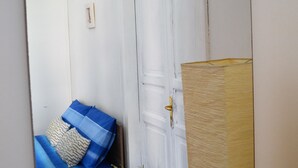 A room with a white door, a blue sofa with patterned cushions, and a small white table with a potted plant. - Hostel Via Zara (Palermo)