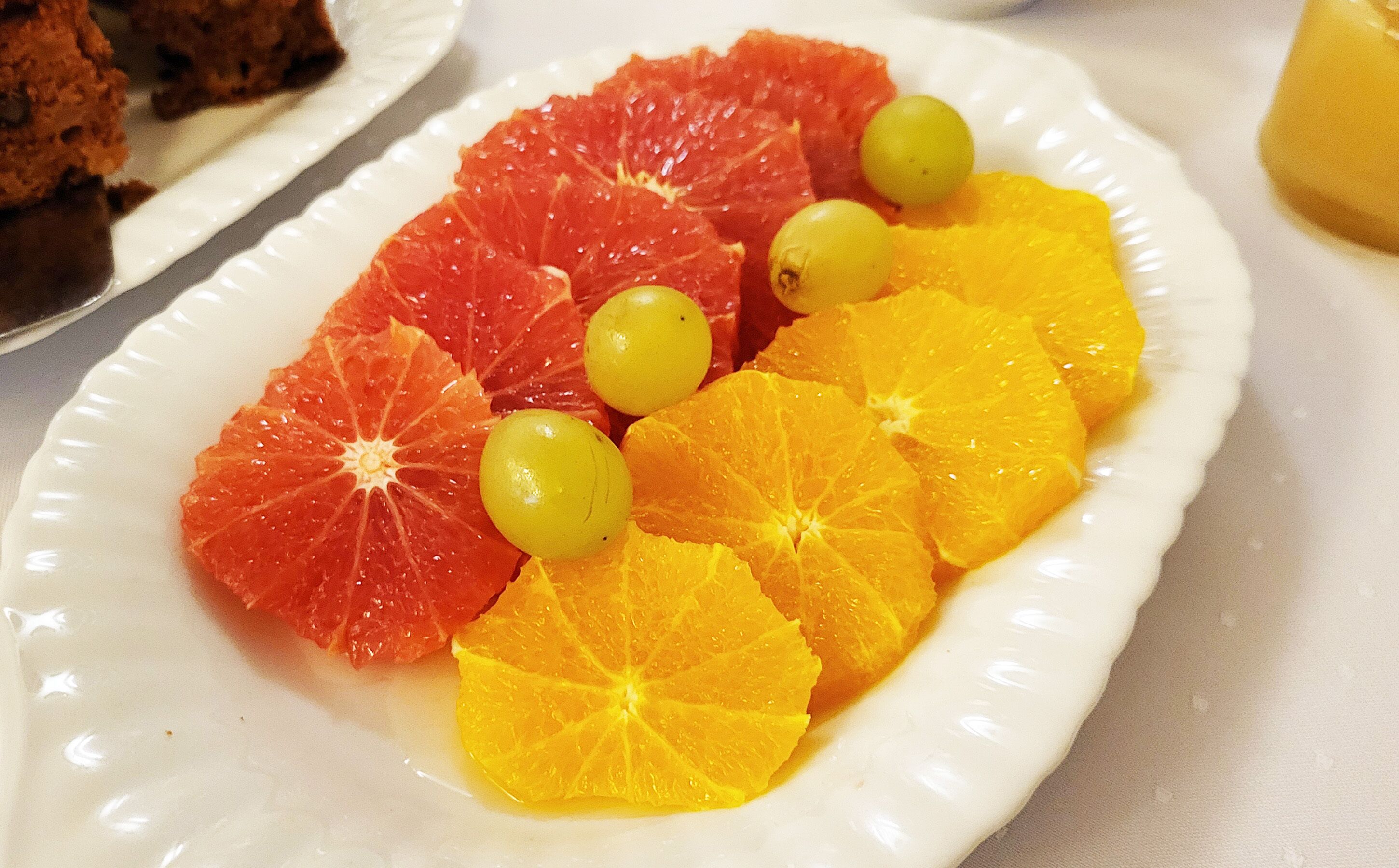 Un plato blanco con rodajas de naranja y pomelo, y uvas verdes.