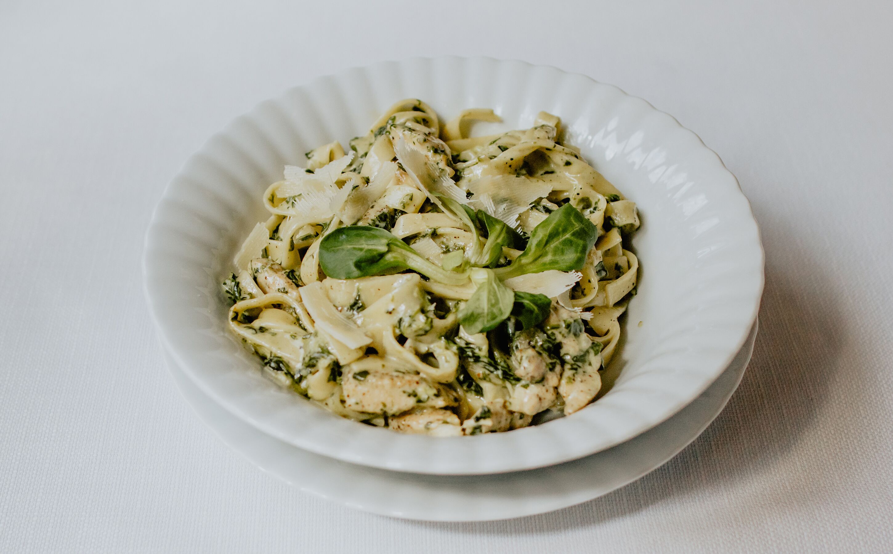 A bowl of pasta with a creamy sauce and fresh basil leaves.