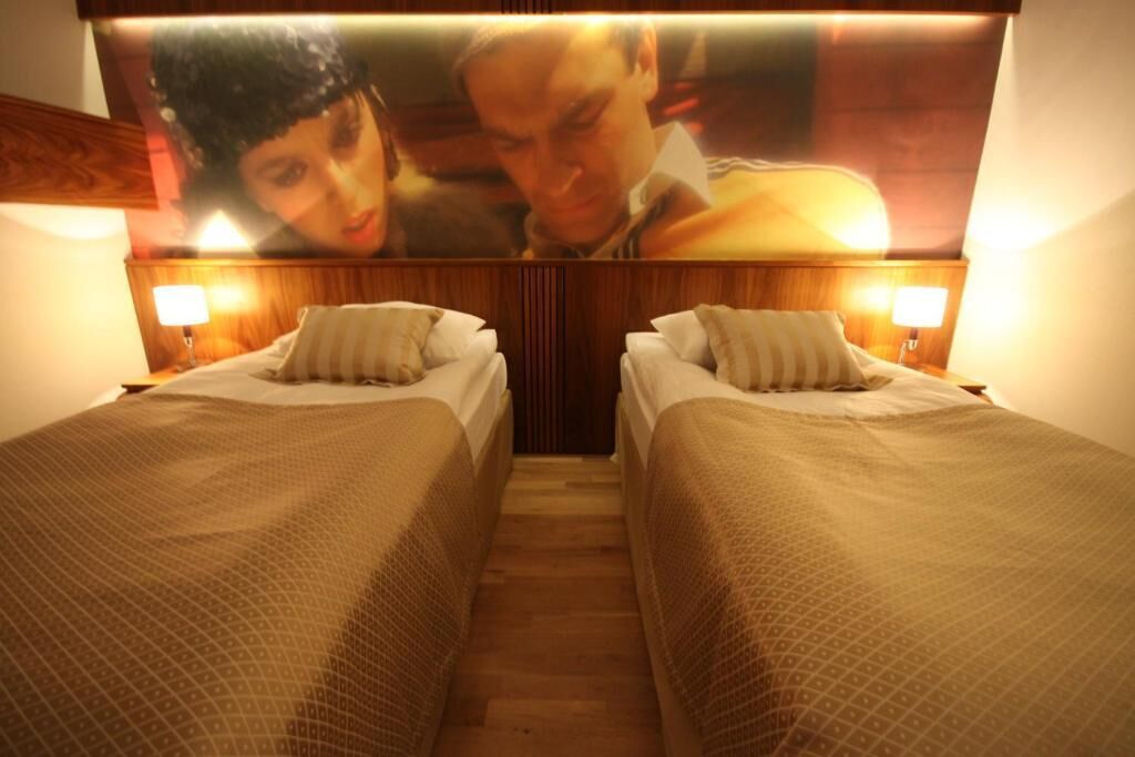A hotel room with two single beds, wooden headboard, and a large poster above the beds.