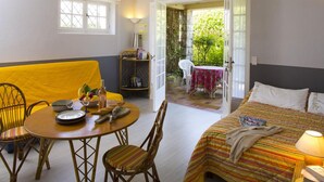 A room with a bed, a dining table with chairs, a small balcony with a table and chairs, and a bookshelf.