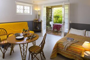 Una habitación con una cama, una mesa de comedor con sillas, un pequeño balcón con una mesa y sillas, y una estantería.