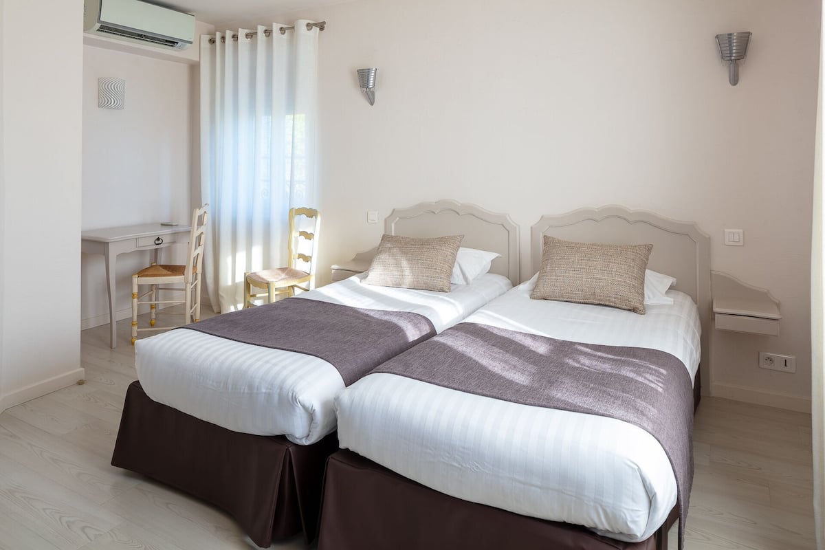 A double bed with a headboard, a desk, a chair, and a window with curtains.