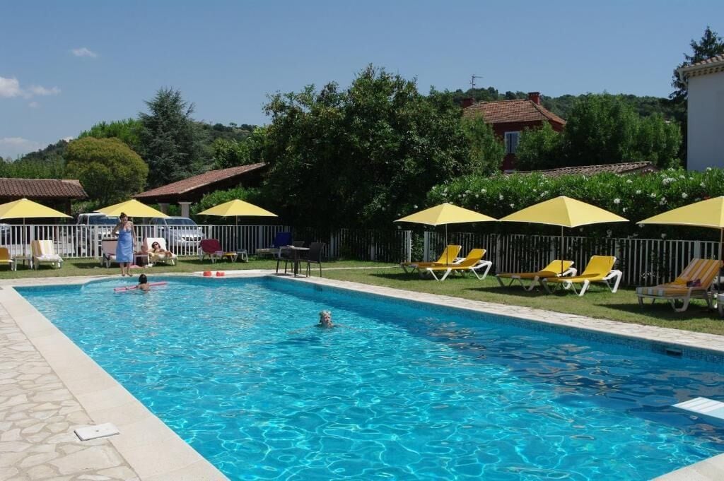 A swimming pool with yellow umbrellas and lounge chairs, surrounded by a fence and greenery.