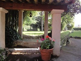 Un espacio al aire libre techado con un banco de piedra, una planta en maceta con flores y un farol colgante.