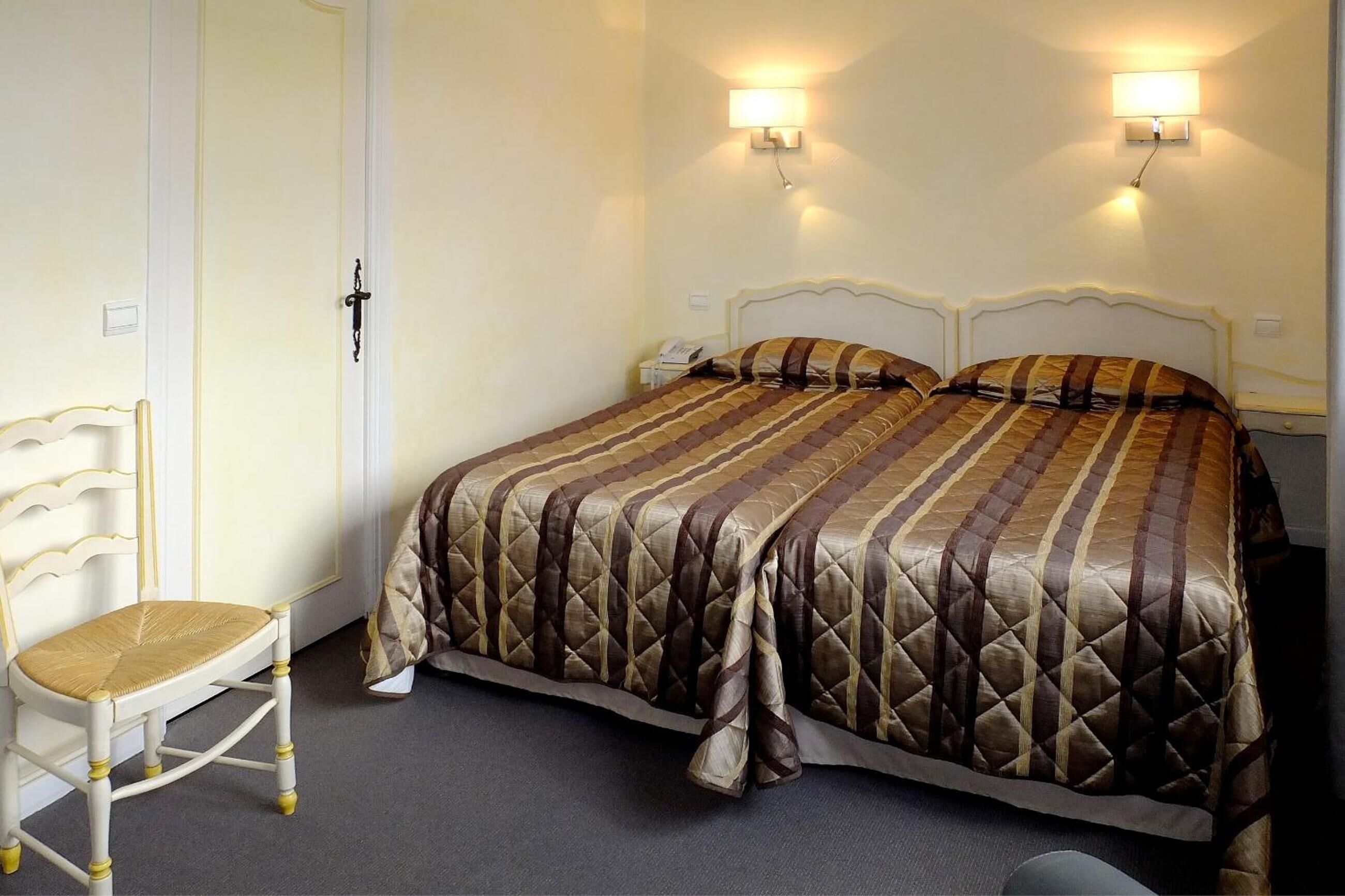 A hotel room with a bed, two bedside lamps, a chair, and a door.