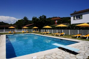 A rectangular swimming pool with a stone border, surrounded by yellow umbrellas and orange lounge chairs. - Hotel Du Bosquet (Pegomas)