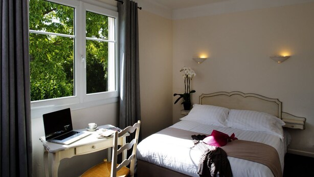 A hotel room with a bed, a desk with a laptop, a chair, and a window with curtains. - Hotel Du Bosquet (Pegomas)