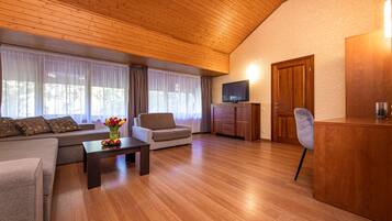 A modern living room with a wooden ceiling, a sofa set, a coffee table with flowers, a TV, and a wooden cabinet.