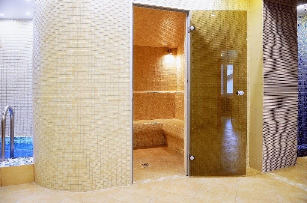 A spa area with a tiled wall, a glass door, and a bench.