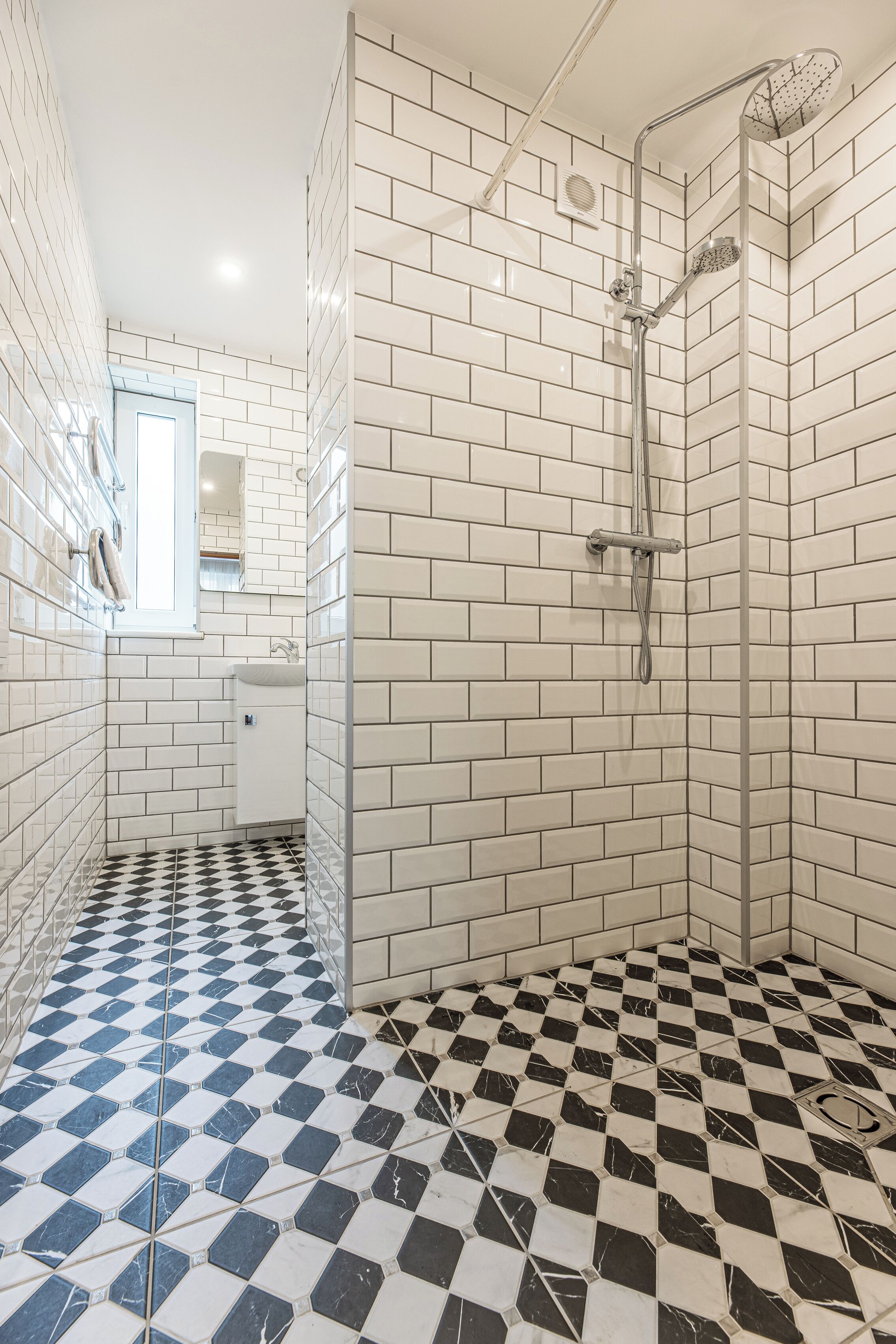 A bathroom with white subway tiles, a black and white checkered floor, a glass shower enclosure, and a small sink with a mirror above it.