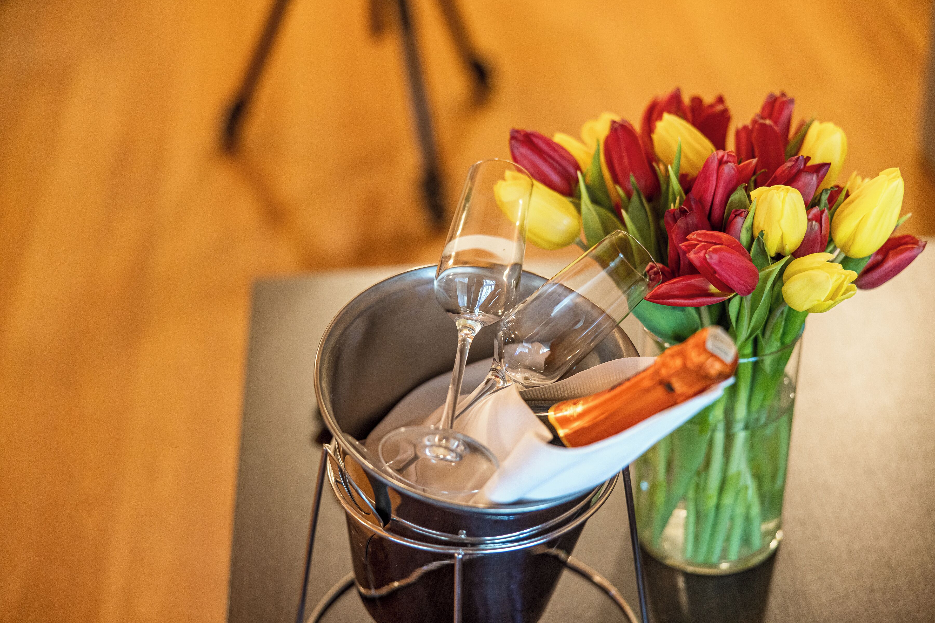 A wine glass in a bucket, a vase with tulips, and a wooden floor.
