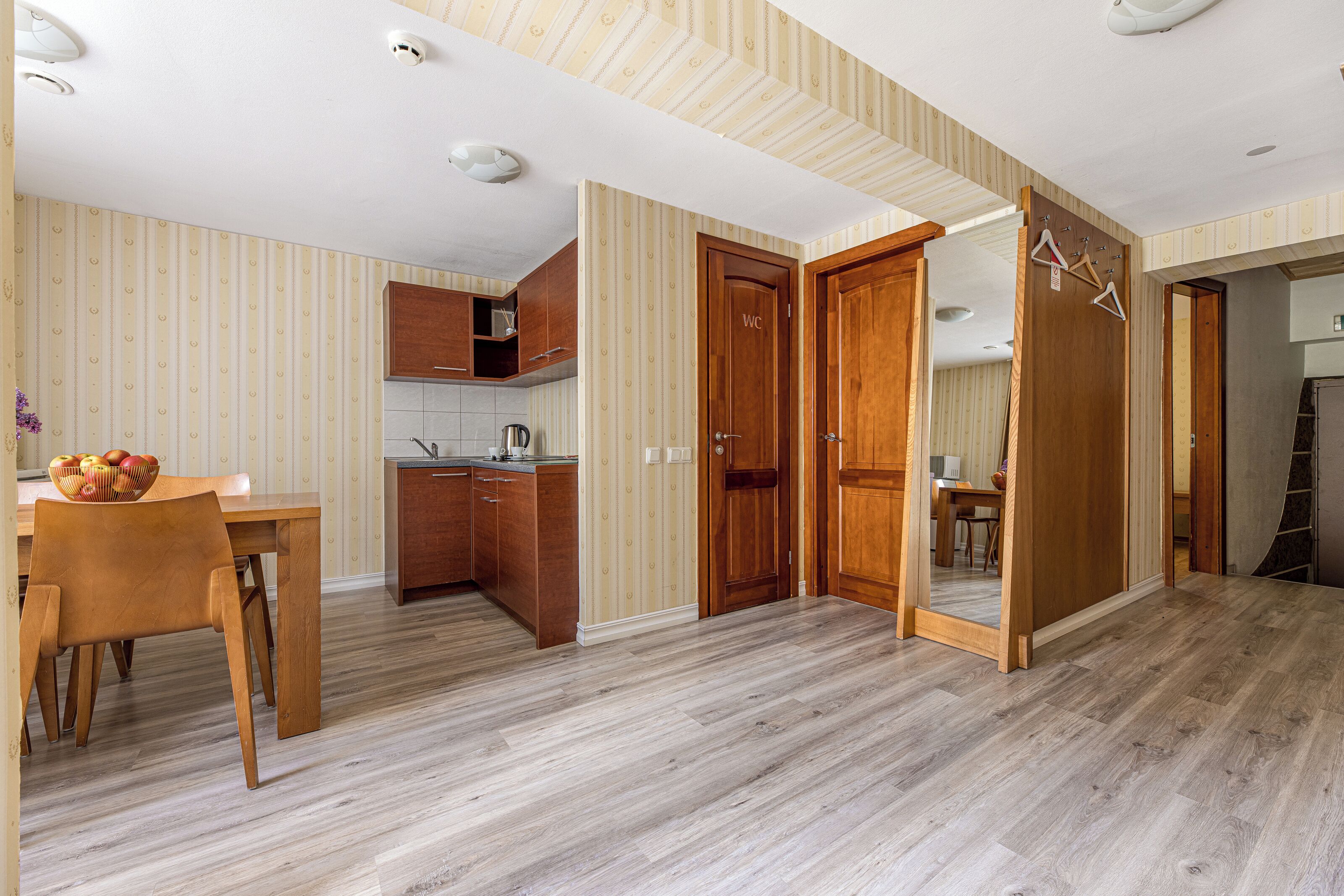 A compact kitchen with wooden cabinets, a dining table with chairs, and a fruit bowl.