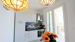 A modern kitchen with white cabinets, a black countertop, and a stove. There are two hanging light fixtures and a vase with sunflowers on the counter. - The Dream Residence 241 (Salve)