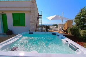 A hot tub with a view of the sea, a staircase to the upper floor, and outdoor seating.