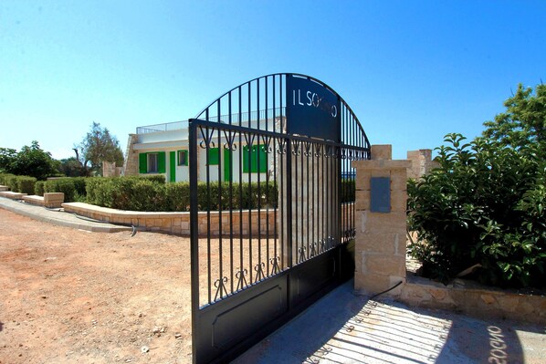 Enter IL SOCIO through a secure, gated entrance surrounded by lush greenery and a beautifully landscaped walkway.