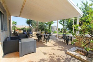 An outdoor patio area with wicker furniture, a covered seating area, and a stone wall. - Casa Saracino (Salve)
