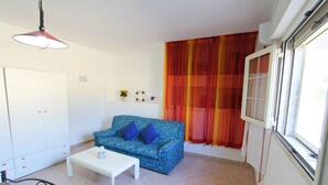 Una sala de estar con un sofá estampado, una mesa de centro blanca y una ventana con cortinas naranjas.
