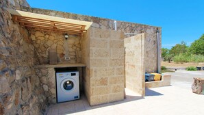 A stone building with a washing machine, a wooden pergola, and a stone bench. - Trullo Saracino (Salve)