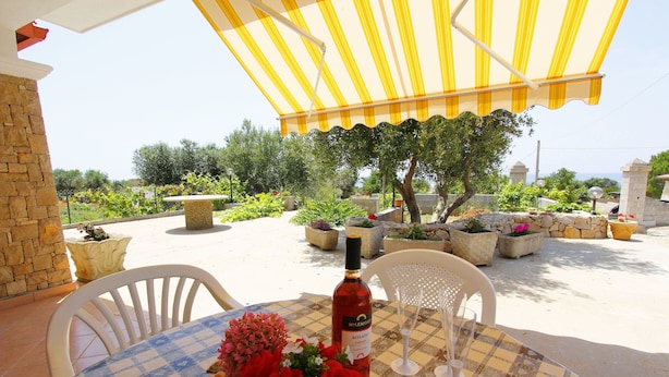 An outdoor dining area with a table set for two, a bottle of rosé wine, and a vase of red flowers. - Villetta 54 (Salve)