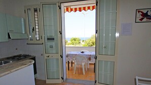 A kitchen with a gas stove, a sink, and a dining area with a table and chairs. - Villetta Rossini (Morciano di Leuca)