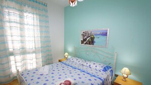 A bedroom with a bed, two bedside tables, a nightstand, a lamp, a curtain, and a wall picture. - Villetta Rossini (Morciano di Leuca)