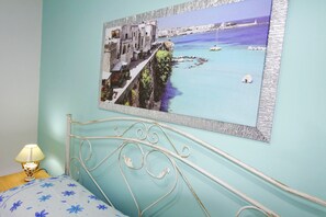 Quarto com uma cama, uma luminária e um quadro com uma paisagem costeira na parede.