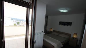 Une chambre à coucher comprenant un lit, des lampes de chevet, une table de chevet, un radiateur, une fenêtre et une vue sur les bâtiments environnants.