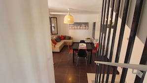 Un salon moderne avec un canapé, une table à manger et des chaises. Un escalier avec une rampe est visible au premier plan.