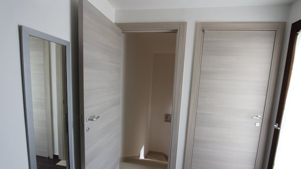 Un couloir avec trois portes, dont une est ouverte et laisse entrevoir un escalier.