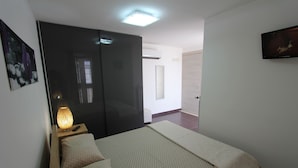 Une chambre à coucher comprenant un lit, une table de chevet, une lampe, une armoire et un téléviseur.