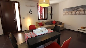 Un salon moderne avec une table à manger, des chaises rouges, un canapé avec des coussins, une grande fenêtre avec des rideaux, une horloge murale et un tableau.