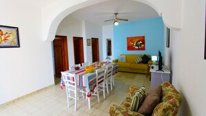 A dining area with a table set for four, a yellow sofa, and a television on a stand. - Villetta Mare 464 (Patu)