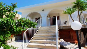 A staircase leading to a white building with arches, a white railing, and a potted plant. - Villetta Mare 464 (Patu)