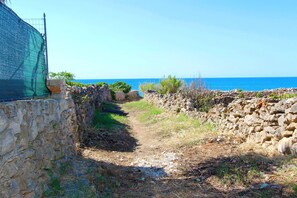 A stone pathway leading to a rocky shoreline with a clear view of the sea.