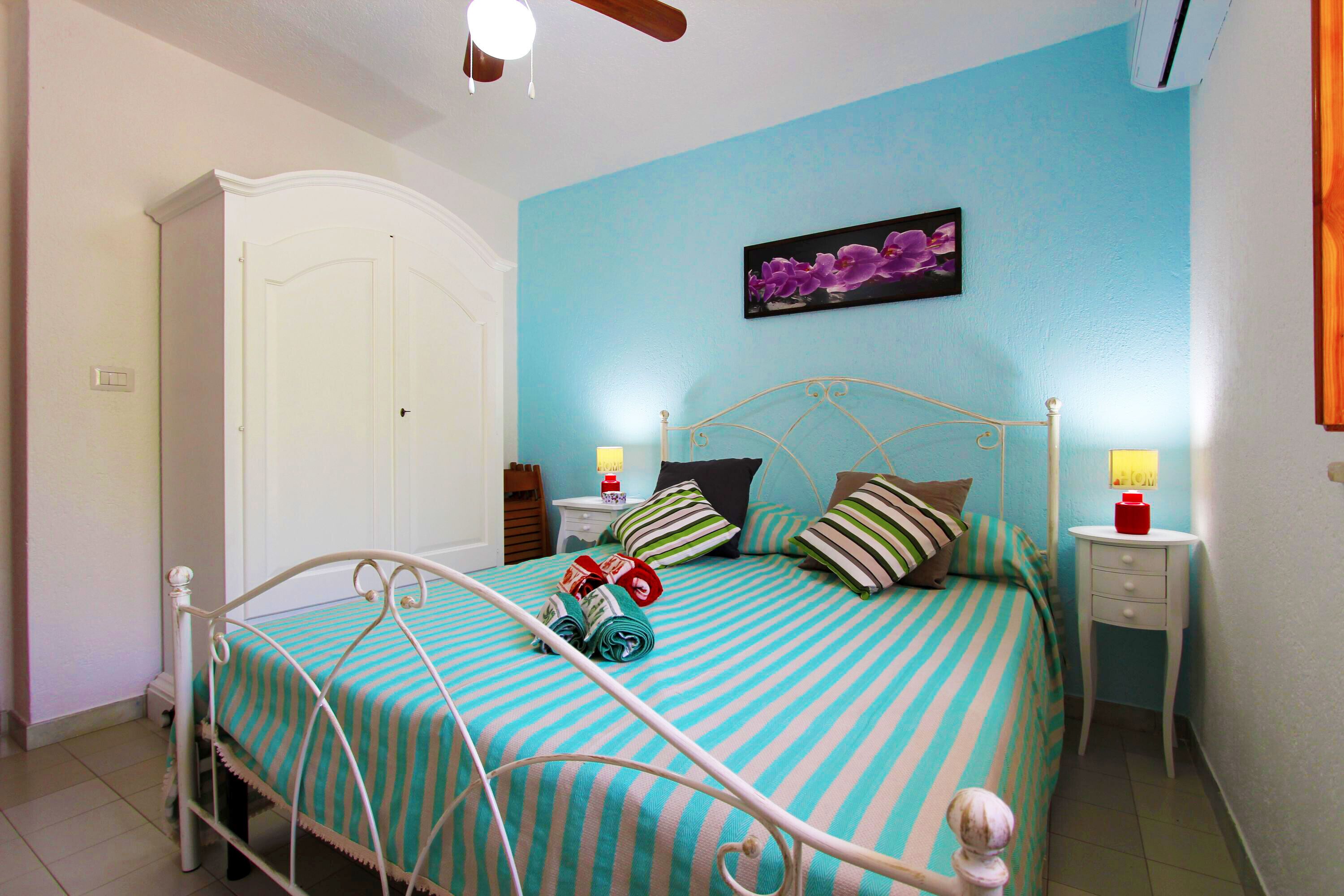 A bedroom with a bed, a nightstand, a lamp, a wardrobe, and a ceiling fan.