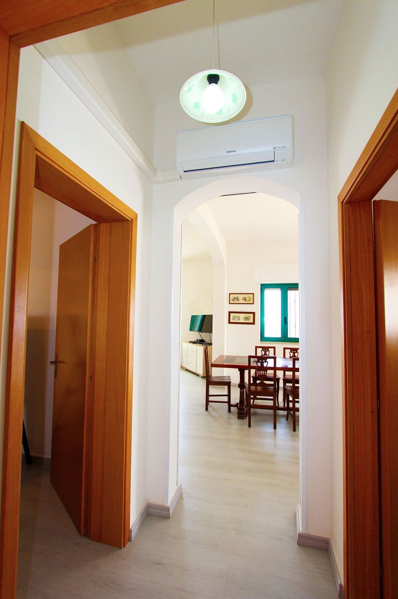 A hallway leading to a dining area with wooden doors, a ceiling light fixture, and an air conditioning unit.