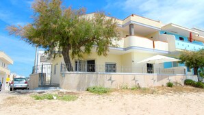 A multi-story building with a balcony, a tree in front, and a parked car. - Beach Apartment in Puglia (Salve)