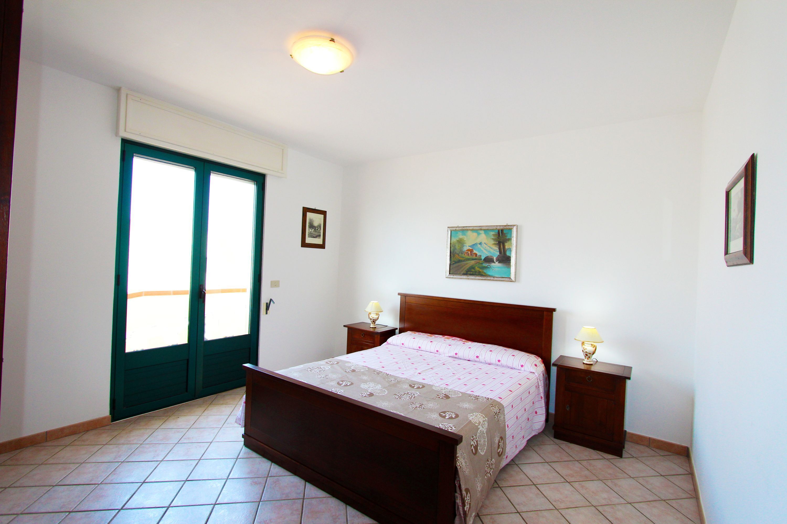 A bedroom with a bed, two bedside tables with lamps, a door, and a painting on the wall.