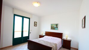 A bedroom with a bed, two bedside tables with lamps, a door, and a painting on the wall. - Beach Apartment in Puglia (Salve)