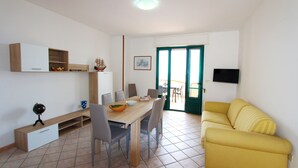A dining area with a wooden table, chairs, and a yellow sofa. - Beach Apartment in Puglia (Salve)