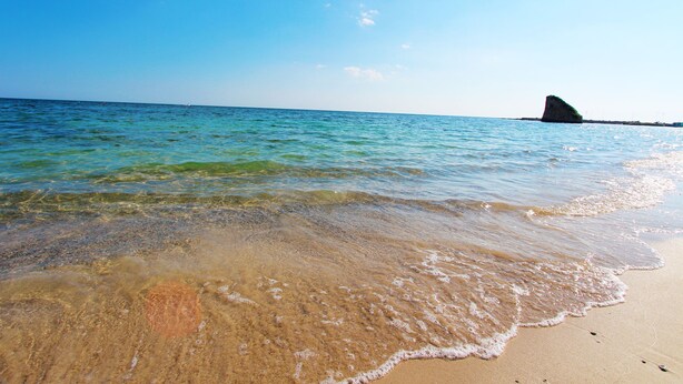 A beach with clear water, a sandy shore, and a rock formation in the distance. - Beach Apartment in Puglia (Salve)
