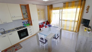 Une cuisine de taille réduite avec des meubles blancs, une cuisinière à gaz et une table à manger avec des chaises.