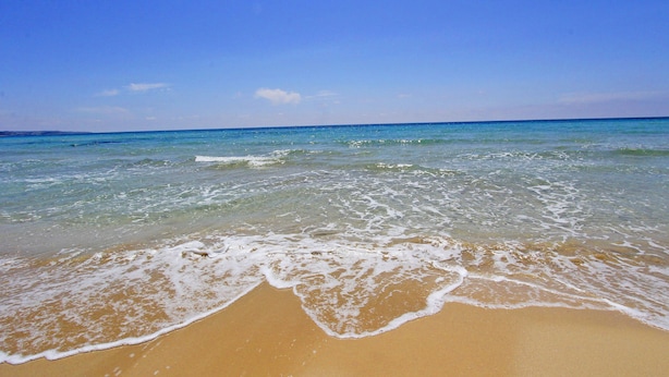Une plage avec une eau d’un bleu limpide et un rivage sablonneux.