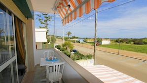 Un balcon avec une table et des chaises, donnant sur une route et des espaces verts.
