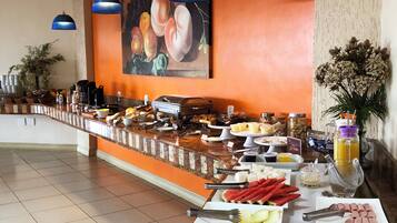 Zona de buffet con una variedad de alimentos, entre ellos frutas, verduras y carnes, y un cuadro de melocotones en la pared.