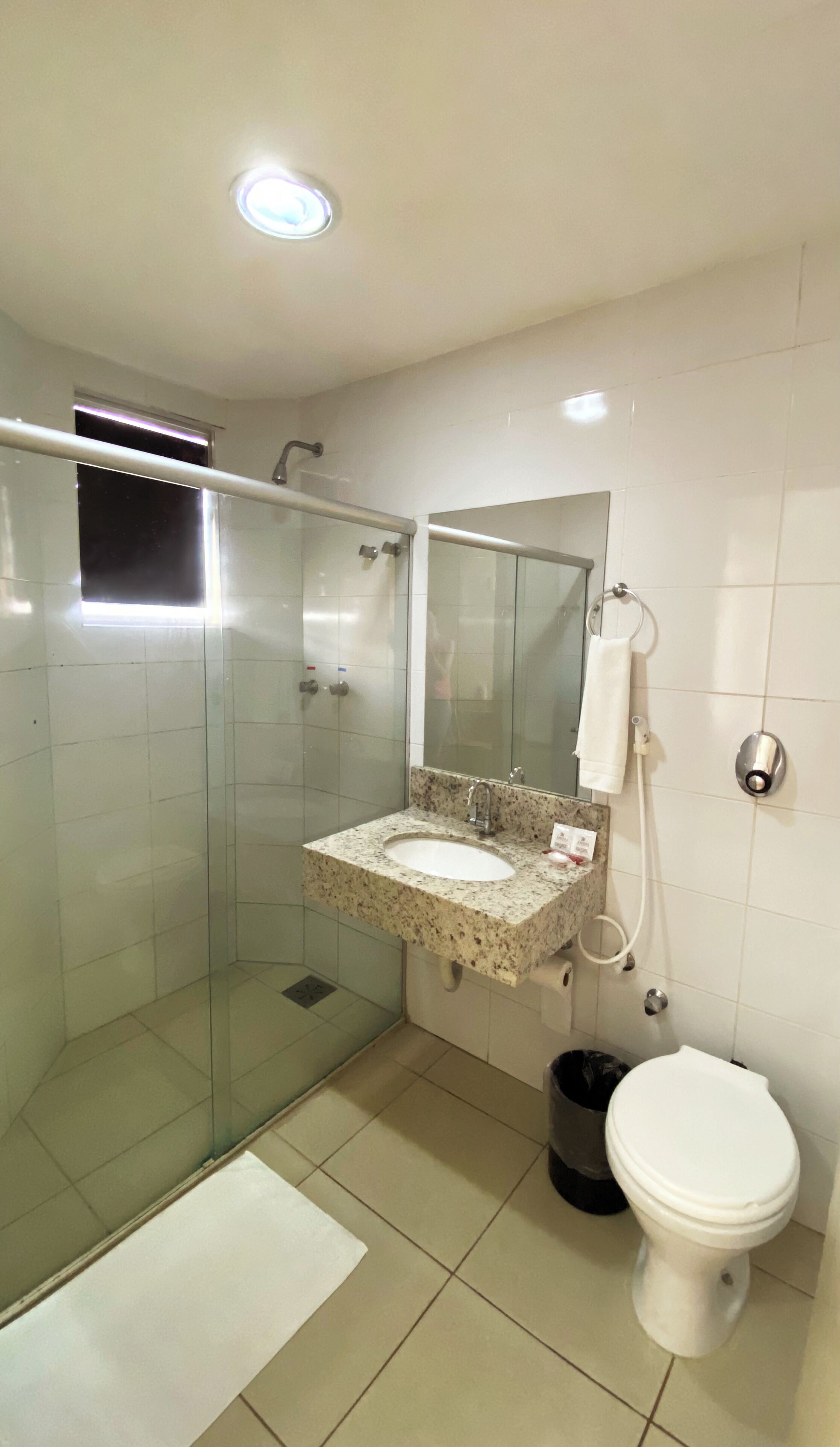Un baño moderno con ducha de vidrio, lavabo con encimera de granito, espejo, toallero y retrete.