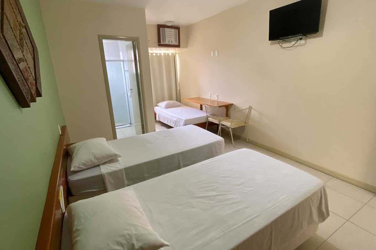 Ein Hotelzimmer mit zwei Betten, einem Schreibtisch, einem Stuhl, einem Fernseher und einer Tür zu einem Balkon.